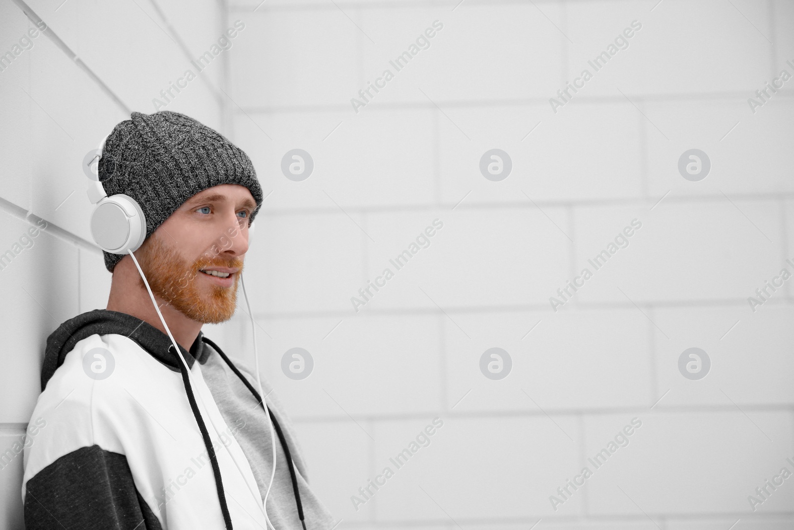 Photo of Young man listening to music with headphones near light wall. Space for text