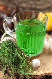 Photo of Aromatic herbal tea, fresh tarragon sprigs and sugar cube on wooden stump, closeup