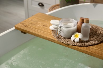 Wooden tray with spa products and stones on bath tub in bathroom. Space for text