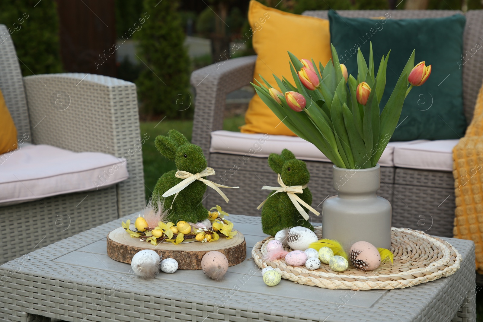 Photo of Terrace with Easter decorations. Bouquet of tulips in vase, bunny figures and decorative eggs on table outdoors