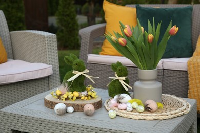 Photo of Terrace with Easter decorations. Bouquet of tulips in vase, bunny figures and decorative eggs on table outdoors