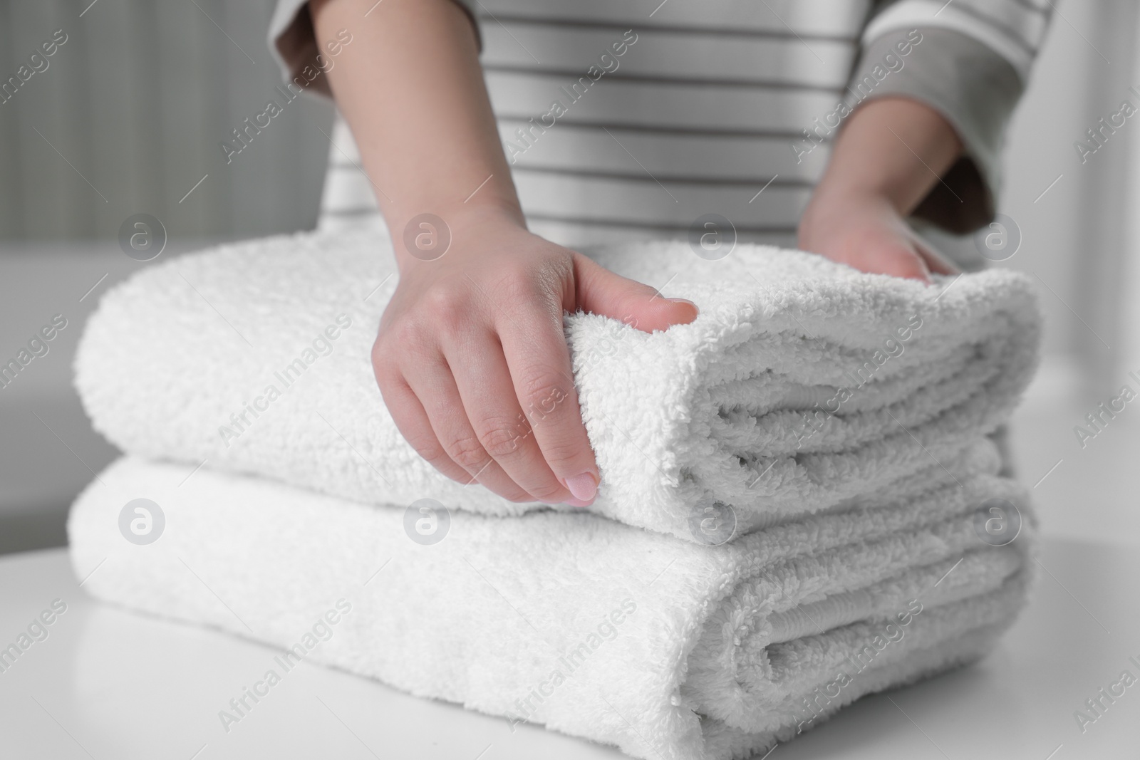 Photo of Woman touching soft white towel indoors, closeup