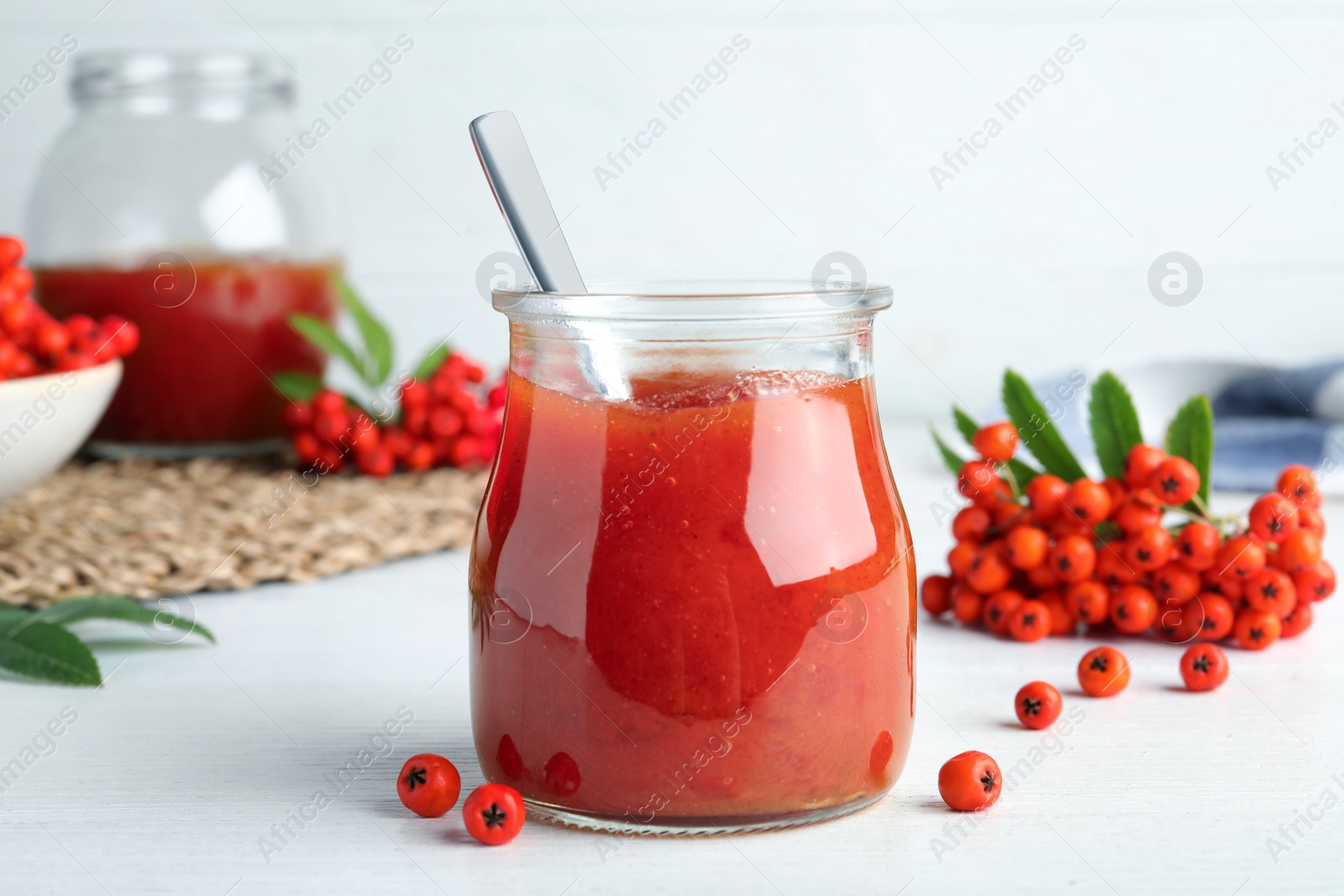 Photo of Delicious rowan jam in glass jar on white wooden table