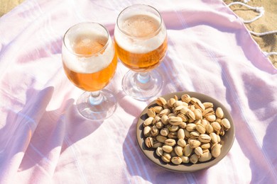 Glasses of cold beer and pistachios on sandy beach, above view