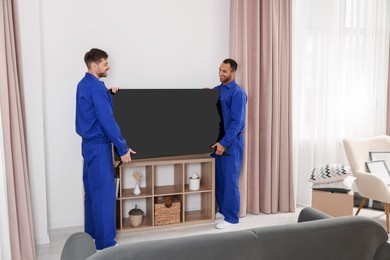 Photo of Male movers installing plasma TV near white wall in new house