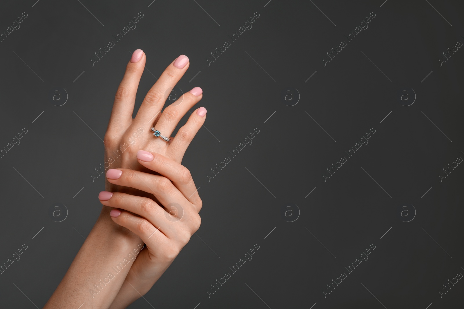 Photo of Woman with elegant ring on dark grey background, closeup. Space for text