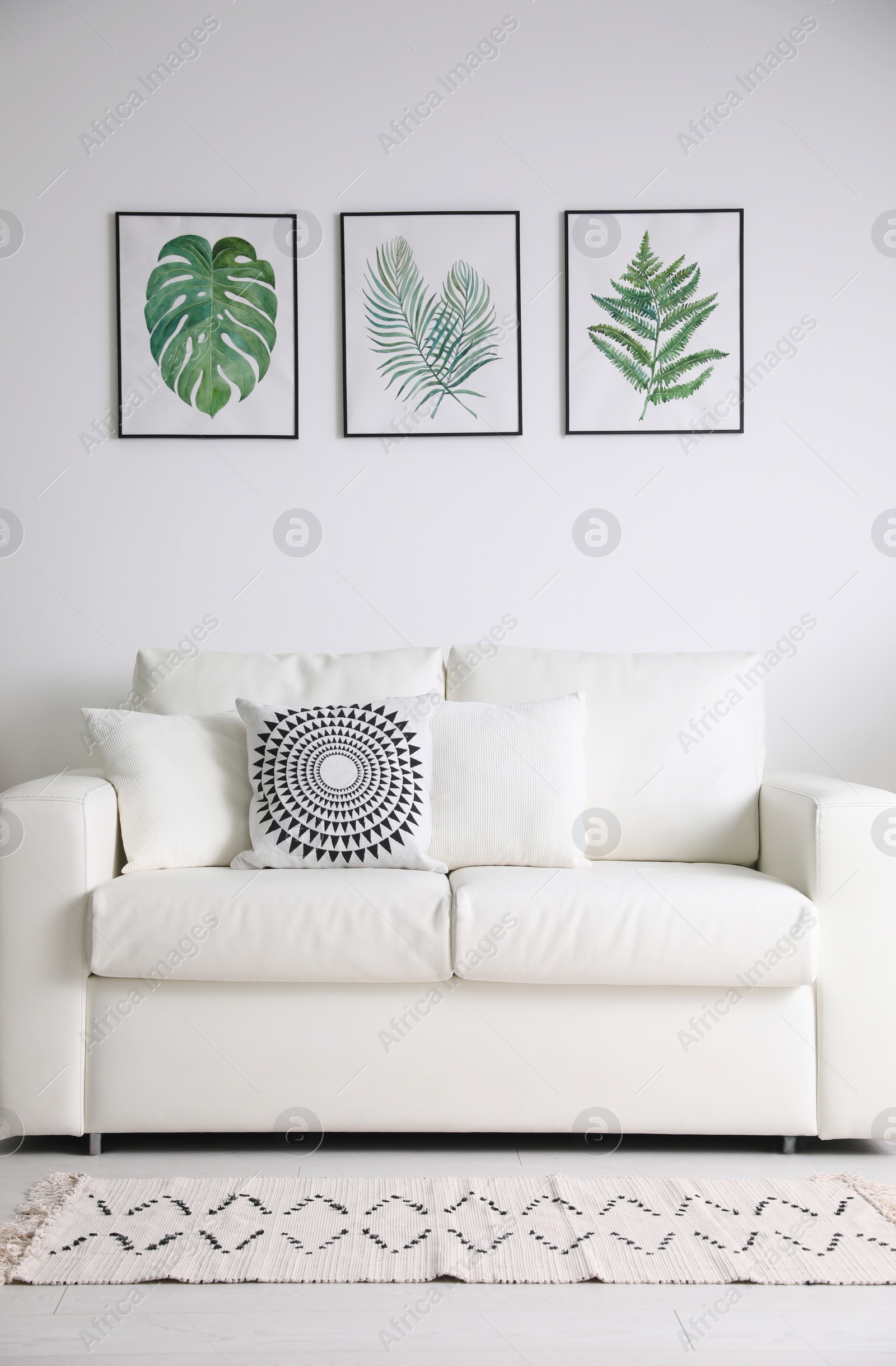 Photo of Beautiful paintings of tropical leaves over sofa in living room interior