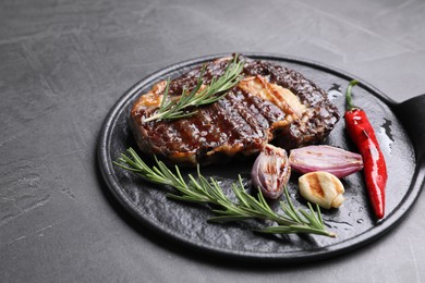 Delicious grilled beef meat, rosemary and spices on gray textured table, space for text