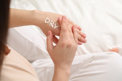 Young woman with word Dry made of cream on her hand on bed, closeup