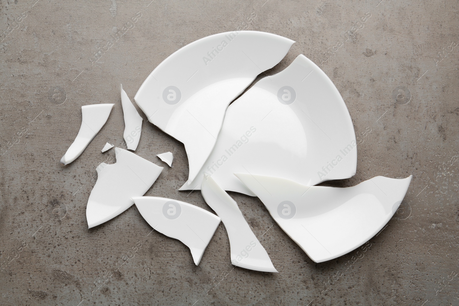 Photo of Pieces of broken ceramic plate on grey table, flat lay