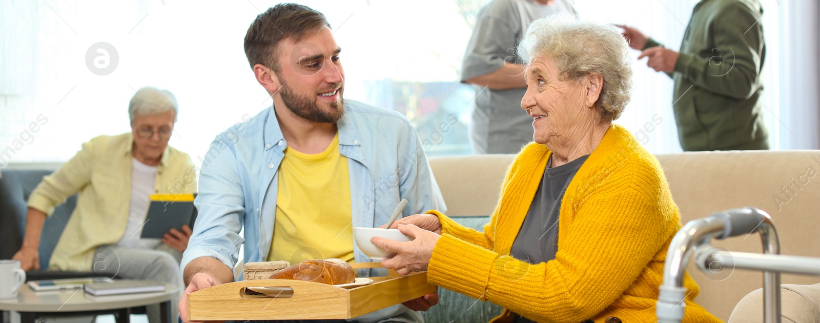 Image of Young man serving dinner for elderly woman in geriatric hospice, banner design. Senior people care