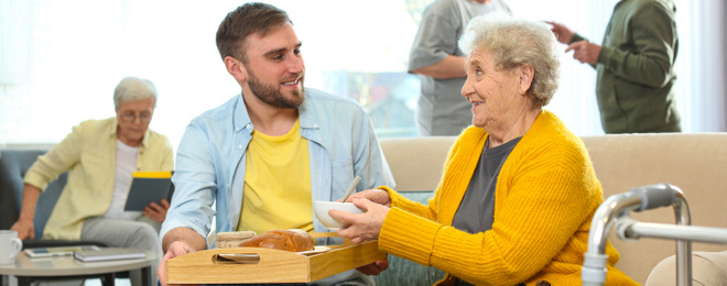 Image of Young man serving dinner for elderly woman in geriatric hospice, banner design. Senior people care