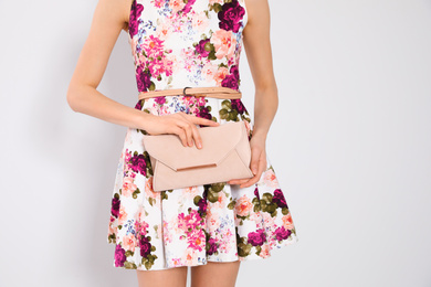 Young woman wearing floral print dress with clutch on light background, closeup