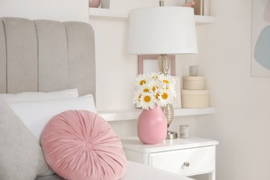 Bouquet of beautiful daisy flowers and lamp on nightstand in bedroom