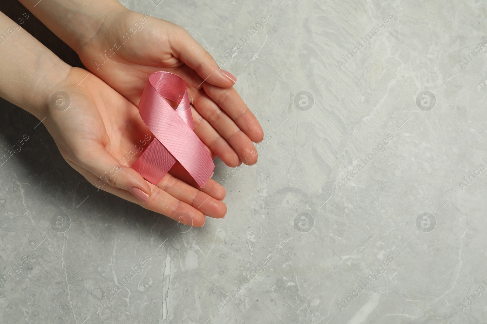 Photo of Breast cancer awareness. Woman with pink ribbon at grey marble table, top view. Space for text