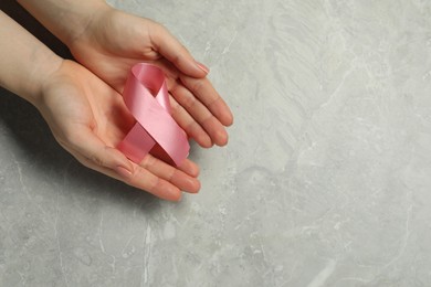 Breast cancer awareness. Woman with pink ribbon at grey marble table, top view. Space for text