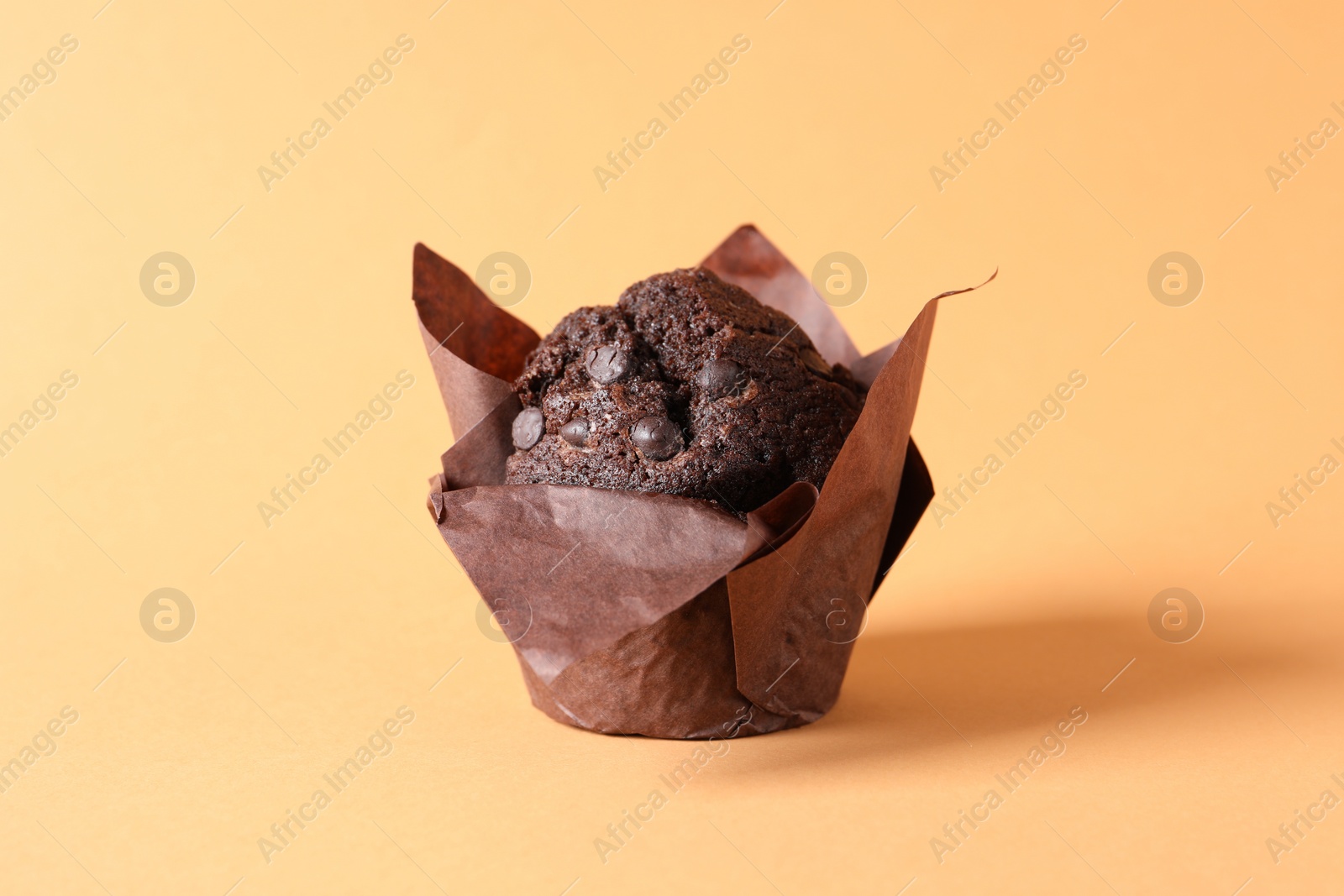 Photo of Tasty chocolate muffin on pale orange background