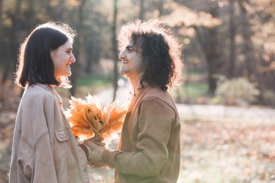 Photo of Happy young couple with dry leaves spending time together in autumn park, space for text. Dating agency