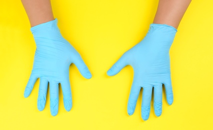 Person in blue latex gloves against yellow background, closeup on hands