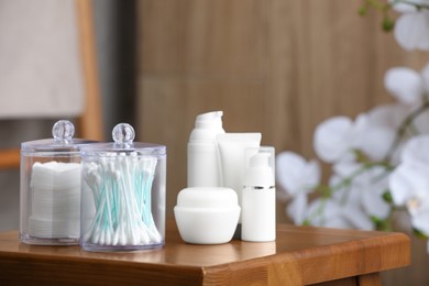 Photo of Cotton pads and swabs near cosmetic products on wooden stool in room