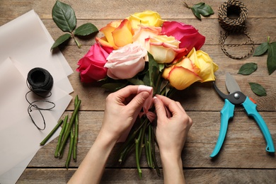 Photo of Woman making luxury bouquet of fresh roses at 
 wooden table, top view