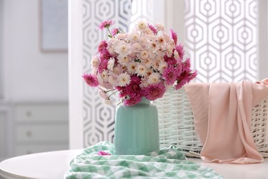 Photo of Vase with beautiful bouquet, wicker basket and checkered cloth on white table in room