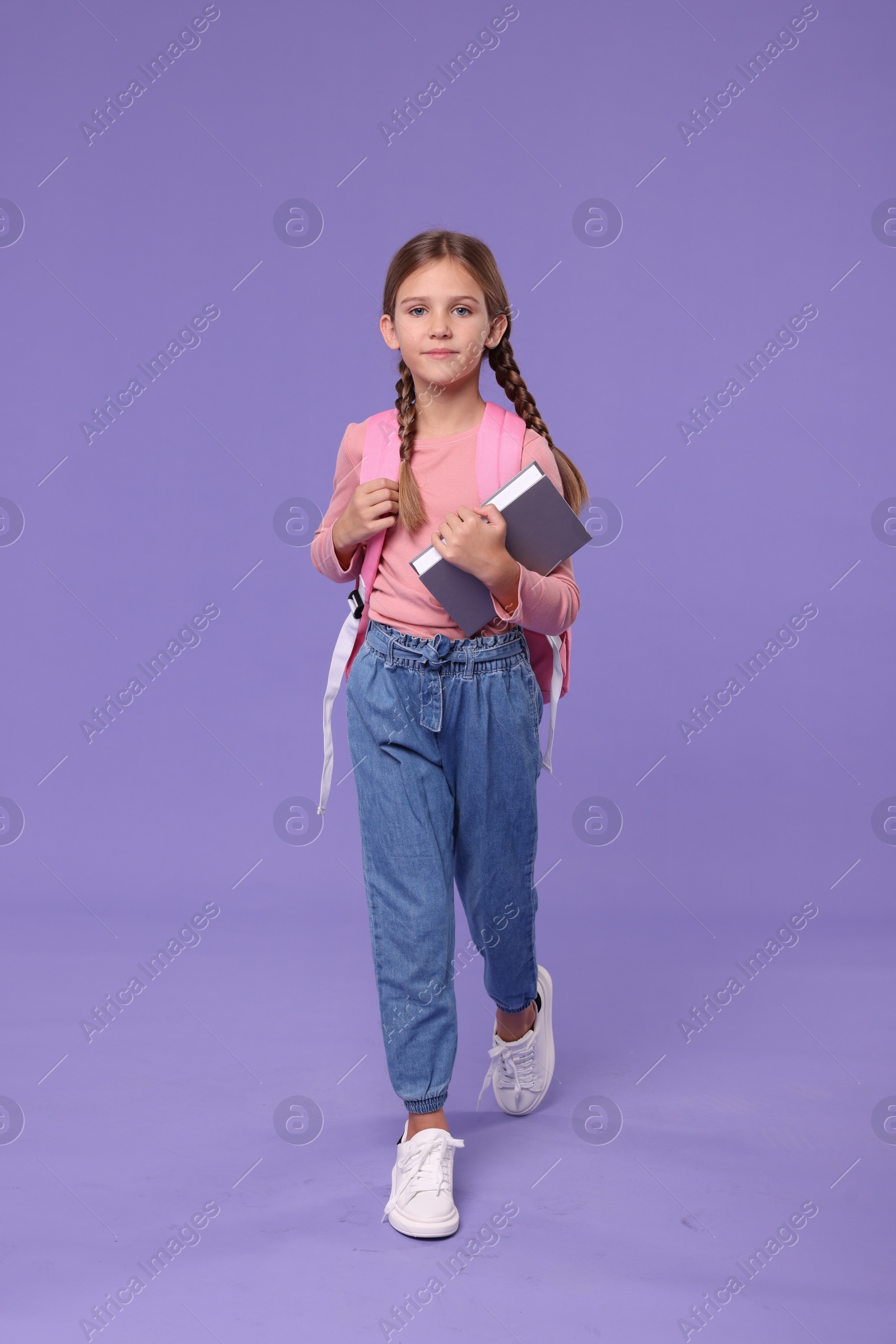 Photo of Cute schoolgirl with books on violet background