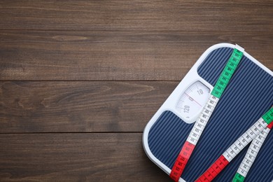 Bathroom scale, measuring tape and space for text on wooden floor, top view. Weight loss concept