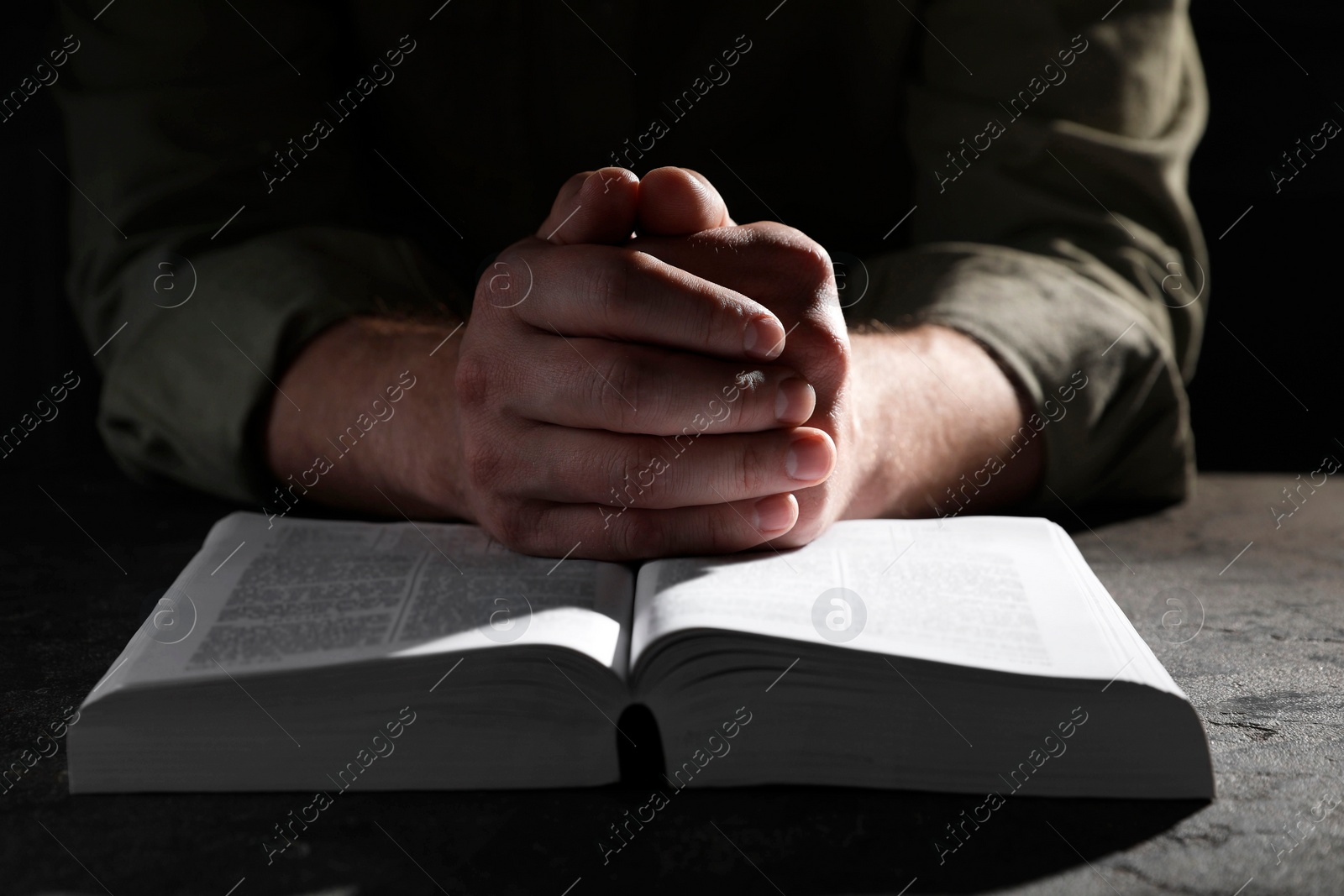 Photo of Religion. Christian man praying over Bible at table, closeup