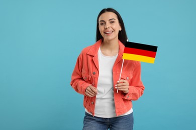 Happy young woman with flag of Germany on light blue background