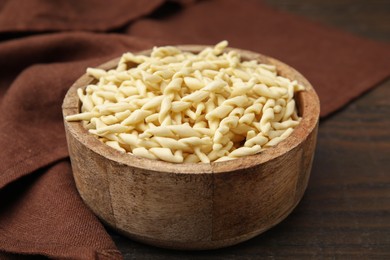 Photo of Uncooked trofie pasta in bowl on wooden table, closeup