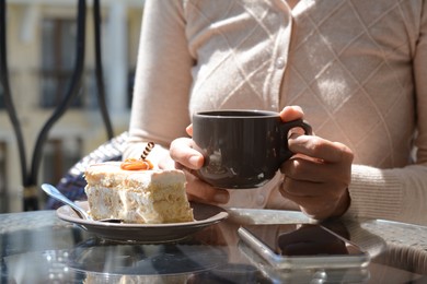 Photo of Woman with cup of coffee and tasty dessert at glass table outdoors, closeup