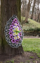 Funeral wreath of plastic flowers on tree outdoors