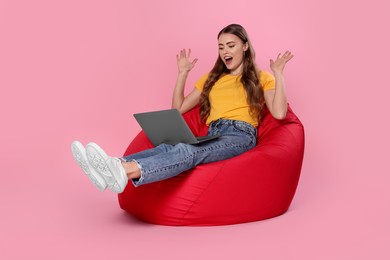 Photo of Emotional woman with laptop sitting on beanbag chair against pink background