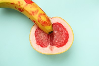 Photo of Banana with red lipstick marks and half of grapefruit on turquoise background, top view. Sex concept
