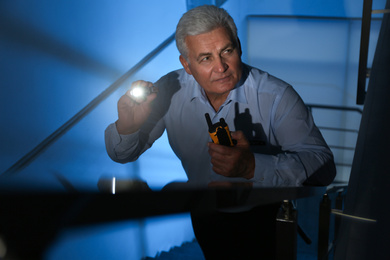 Professional security guard with flashlight on stairs in dark room
