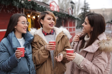 Photo of Happy friends with cups of mulled wine at winter fair