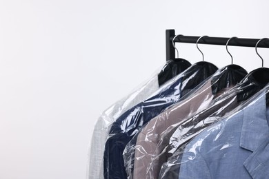 Photo of Dry-cleaning service. Many different clothes in plastic bags hanging on rack against white background, space for text