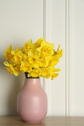 Beautiful daffodils in vase on table near white wall indoors