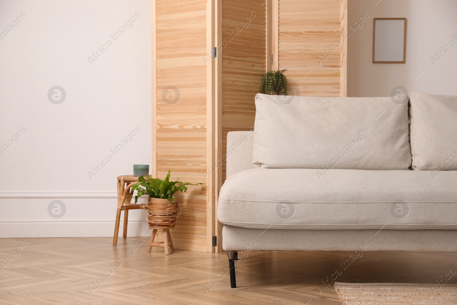 Photo of Stylish room with wooden folding screen and comfortable sofa near white wall. Interior design