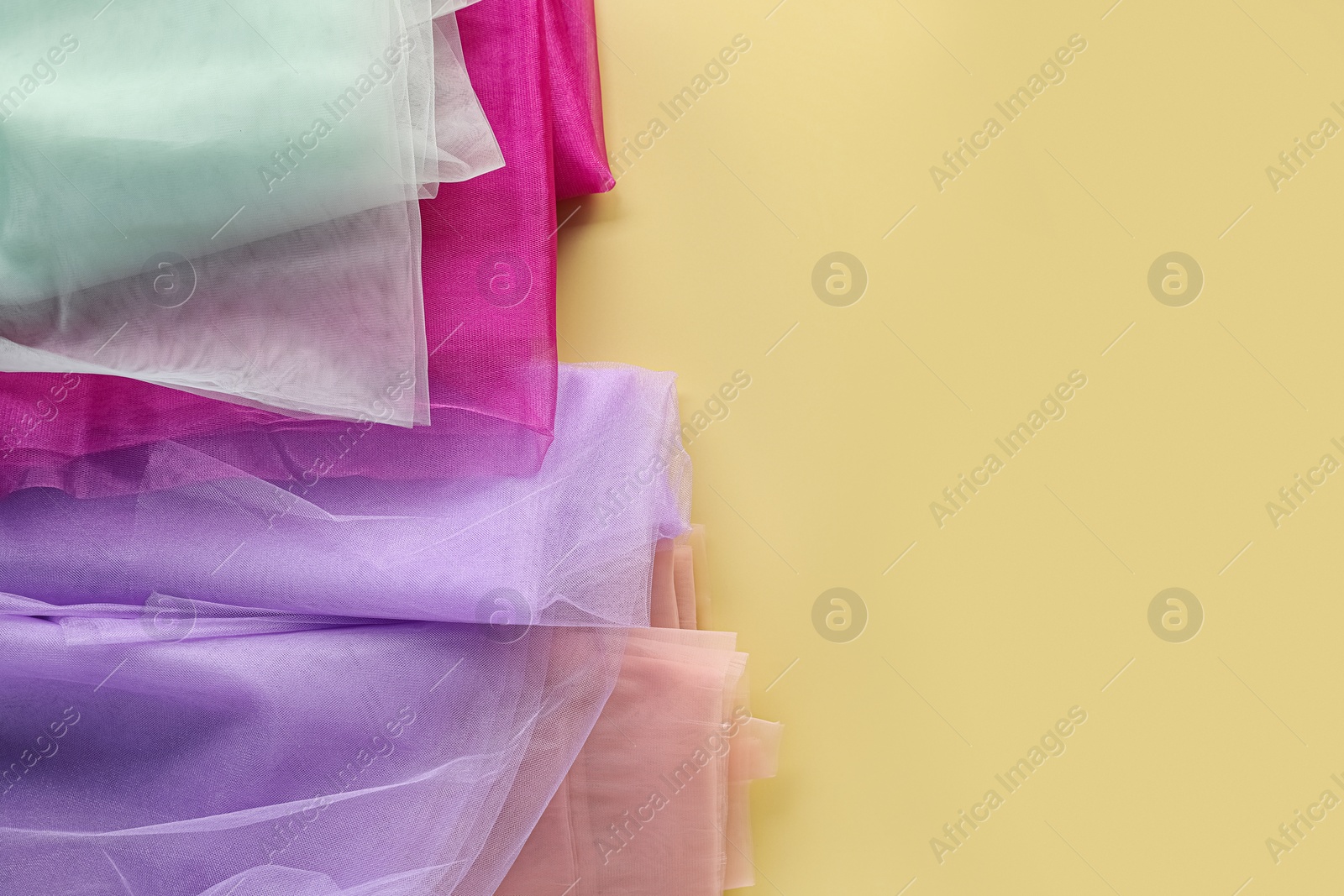 Photo of Beautiful tulle fabrics on yellow background, flat lay. Space for text