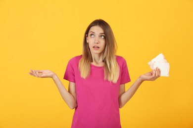 Photo of Thoughtful young woman with disposable menstrual pads on yellow background
