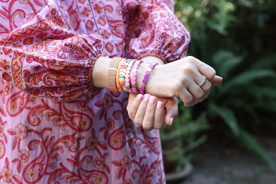 Photo of Woman wearing many stylish bracelets outdoors, closeup