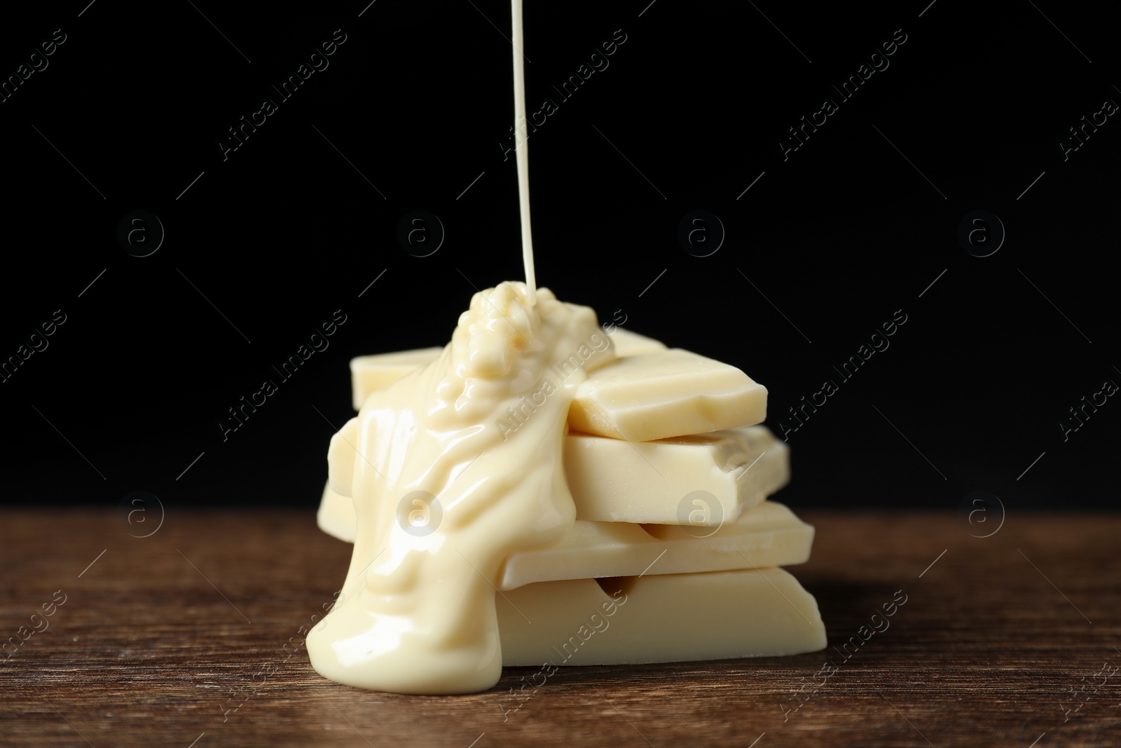 Photo of Pouring tasty white chocolate paste onto pieces on wooden table, closeup