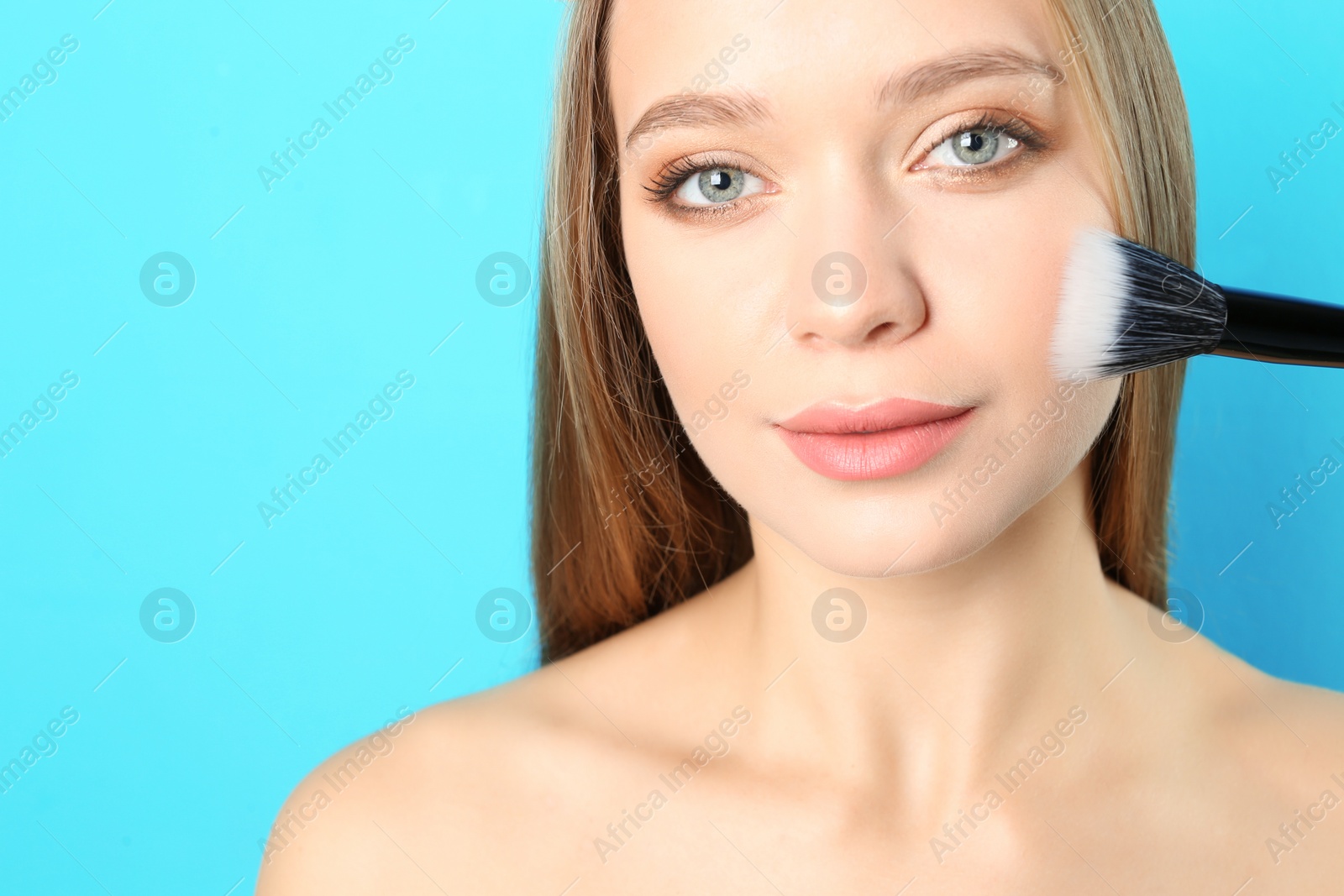 Photo of Portrait of beautiful young woman with makeup brush on color background