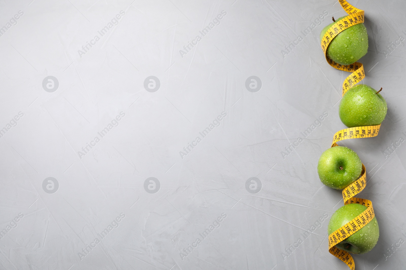 Photo of Ripe green apples and measuring tape on light grey background, flat lay. Space for text