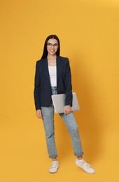 Photo of Young woman with modern laptop on yellow background