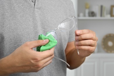 Photo of Man wiping glasses with microfiber cloth indoors, closeup