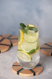 Photo of Glass of lemonade and stylish wooden cup coasters on light table