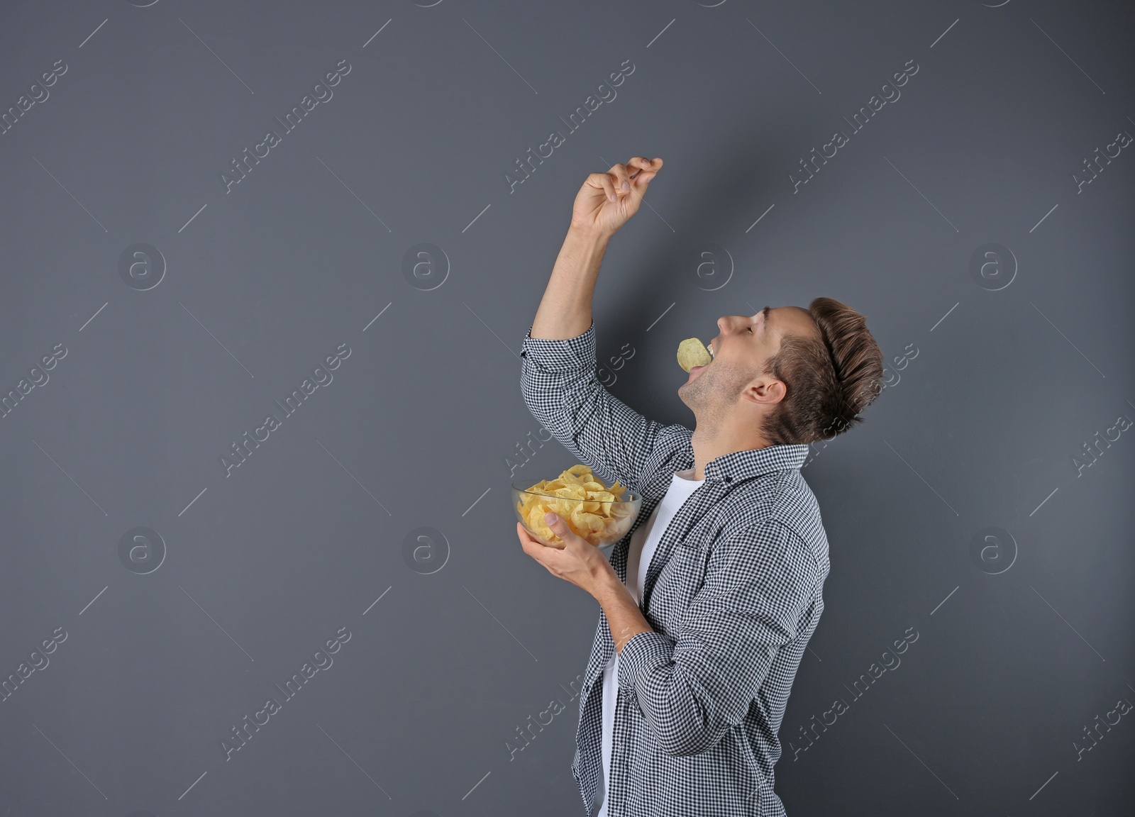 Photo of Man eating potato chips on grey background. Space for text